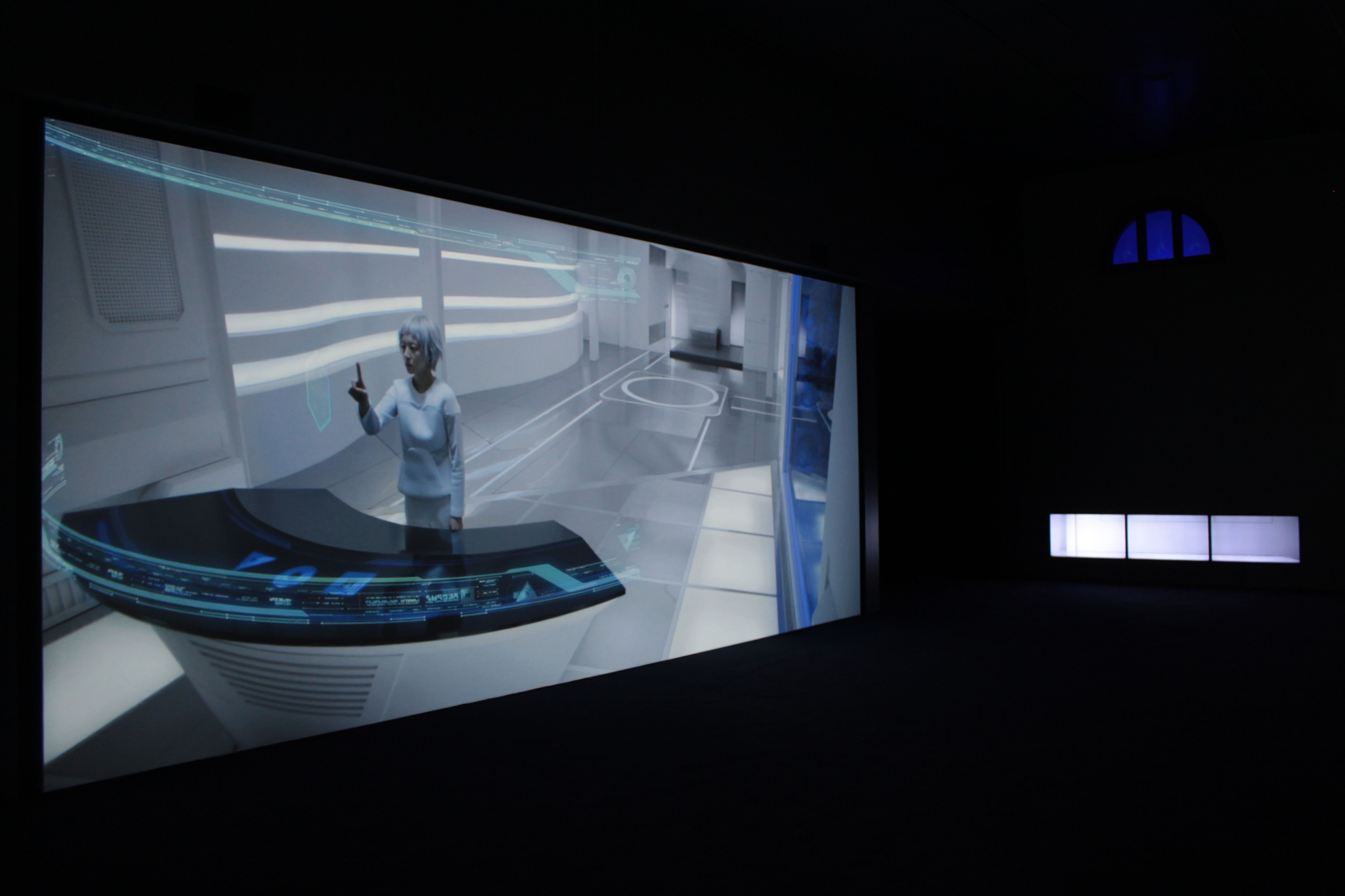 A projected image of an individual dressed in white, situated in a well-lit laboratory environment, holds their index fing...
