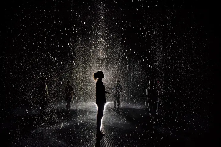 A dark room where silhouettes of multiple individuals are made visible by a spotlight. The central silhouette is prominent...