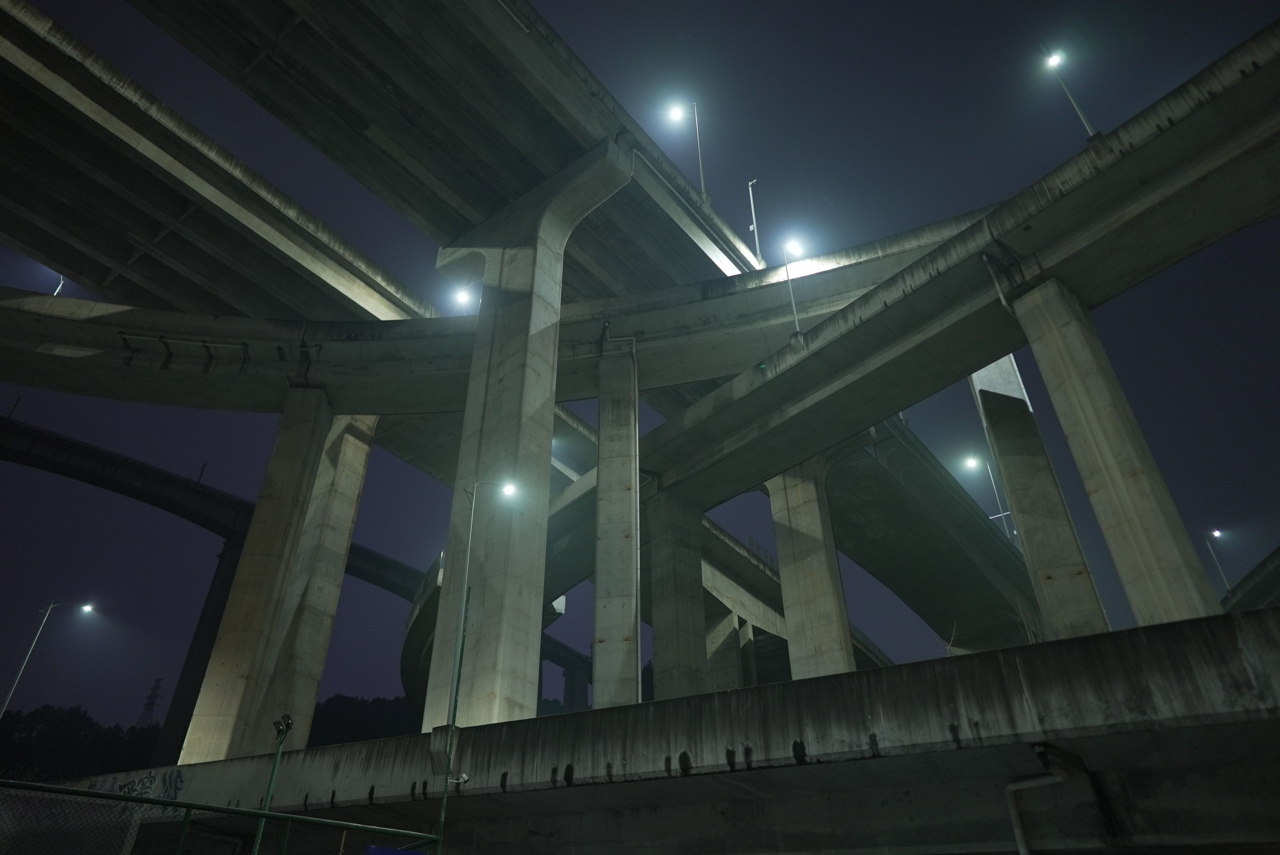 A nighttime photo is captured from a frog’s perspective, showcasing a towering infrastructure of roads in heights. Strikin...