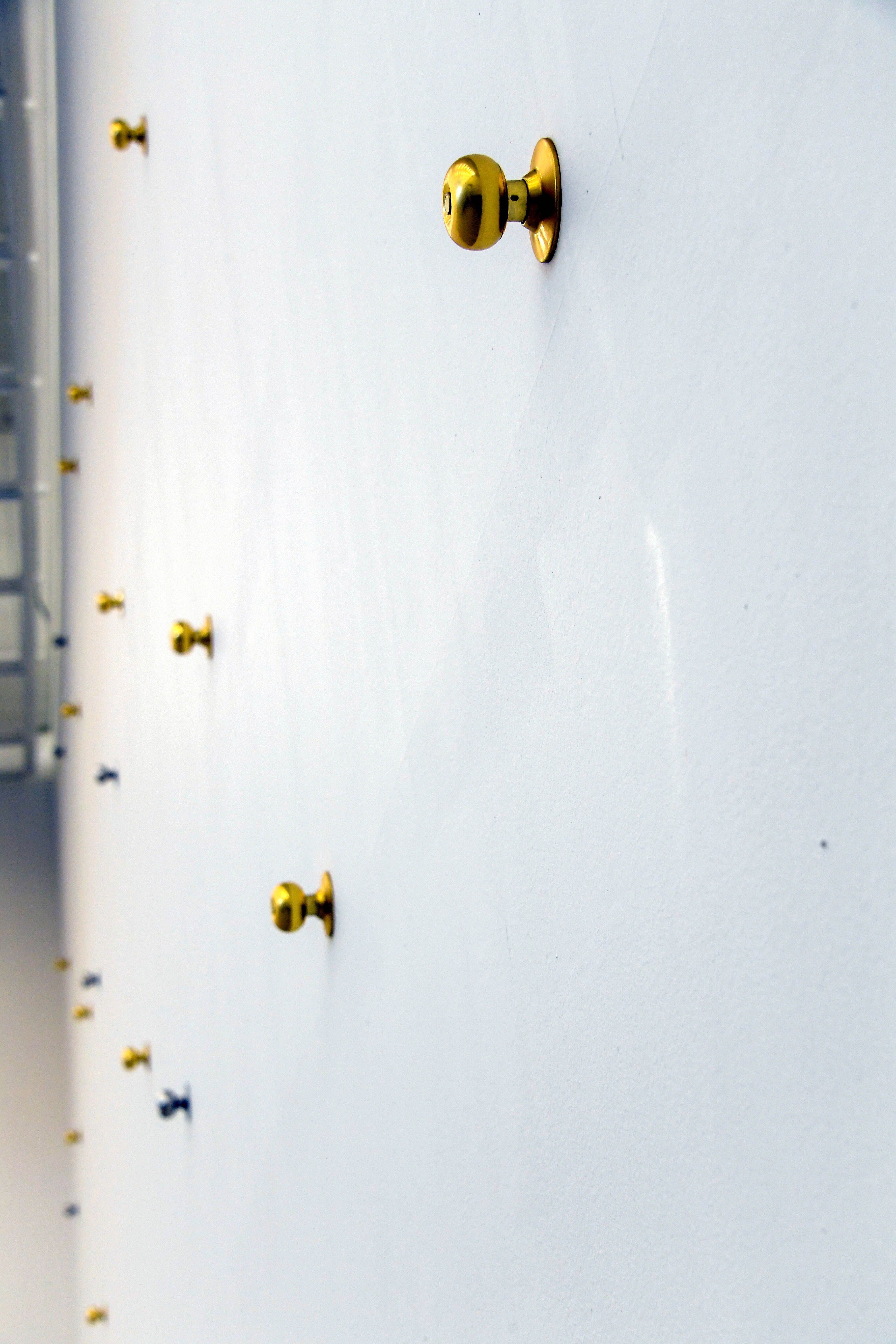 Silver and gold door handles artistically affixed to a pristine white floor in an exhibition space.