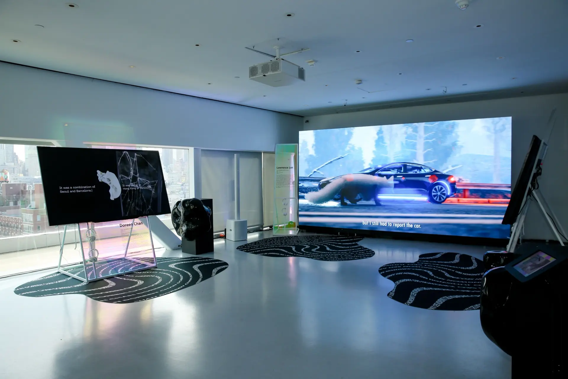 An enormous screen in a room displaying a footage of a driving car, surrounded by black and white posters.