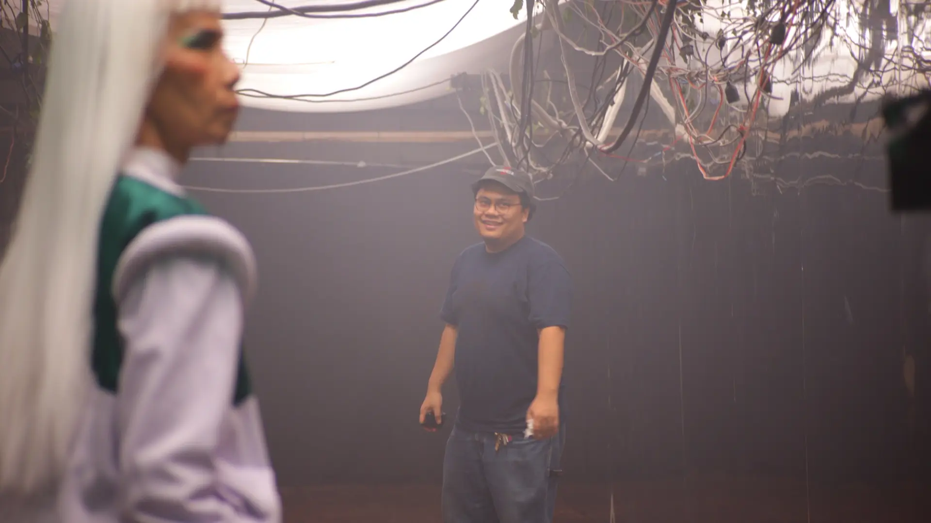 Two individuals stand under a brightly lit ceiling strewn with hanging cords.