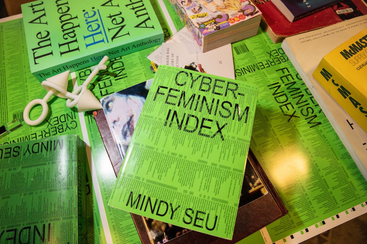 A table of books, including "Cyber Feminism Index" by Mindy Seu, with vibrant green and black covers.