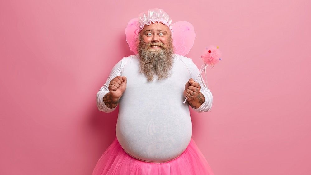 uomo vestito da fata sorride con bacchetta magica in mano e tutu.jpg