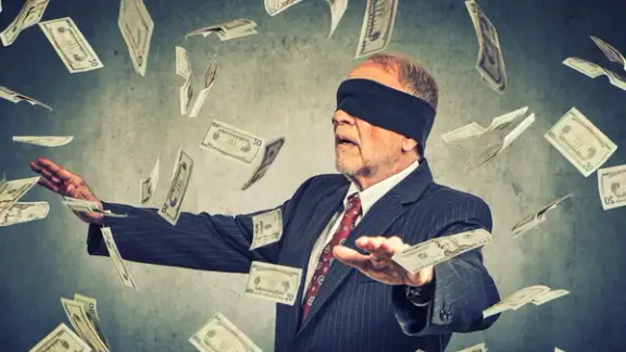 Blindfolded senior businessman trying to catch dollar bills banknotes flying in the air on gray wall background. Financial corporate success or crisis challenge concept-1.jpeg