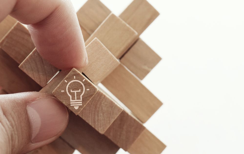 close up of hand showing illuminated light bulb icon on a wooden block puzzle as innovation concept.jpeg