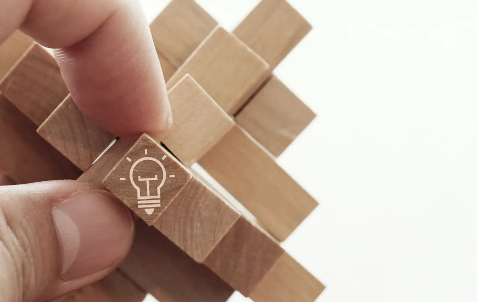 close up of hand showing illuminated light bulb icon on a wooden block puzzle as innovation concept.jpeg