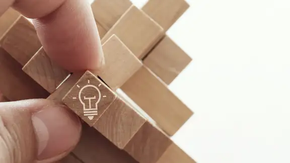 close up of hand showing illuminated light bulb icon on a wooden block puzzle as innovation concept.jpeg
