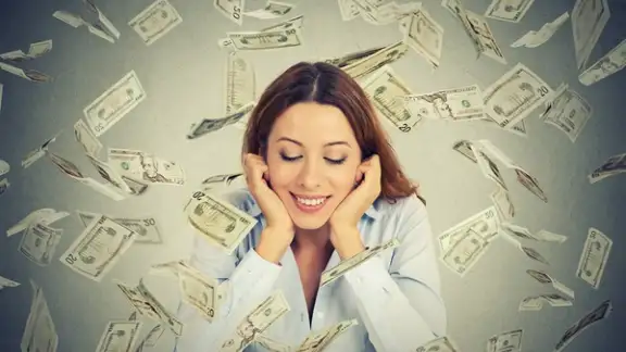 Excited happy young woman sitting at table with growing stack of coins under a money rain isolated on gray wall background. Positive emotions financial success luck good economy concept.jpeg