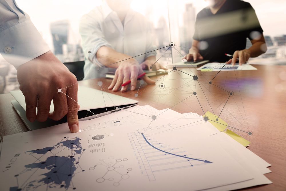 business documents on office table with smart phone and laptop computer and graph financial with social network diagram and two colleagues discussing data in the background.jpeg