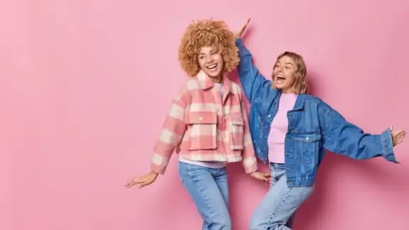 indoor-shot-of-happy-carefree-beautiful-young-women-wear-fashionable-clothes-dance-with-arms-raised-up-move-against-pink-background-blank-copy-space-for-your-promotional-content-lets-party.jpg