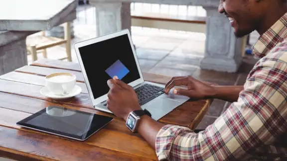 Man doing online shopping with credit card on laptop in cafeteria.jpeg