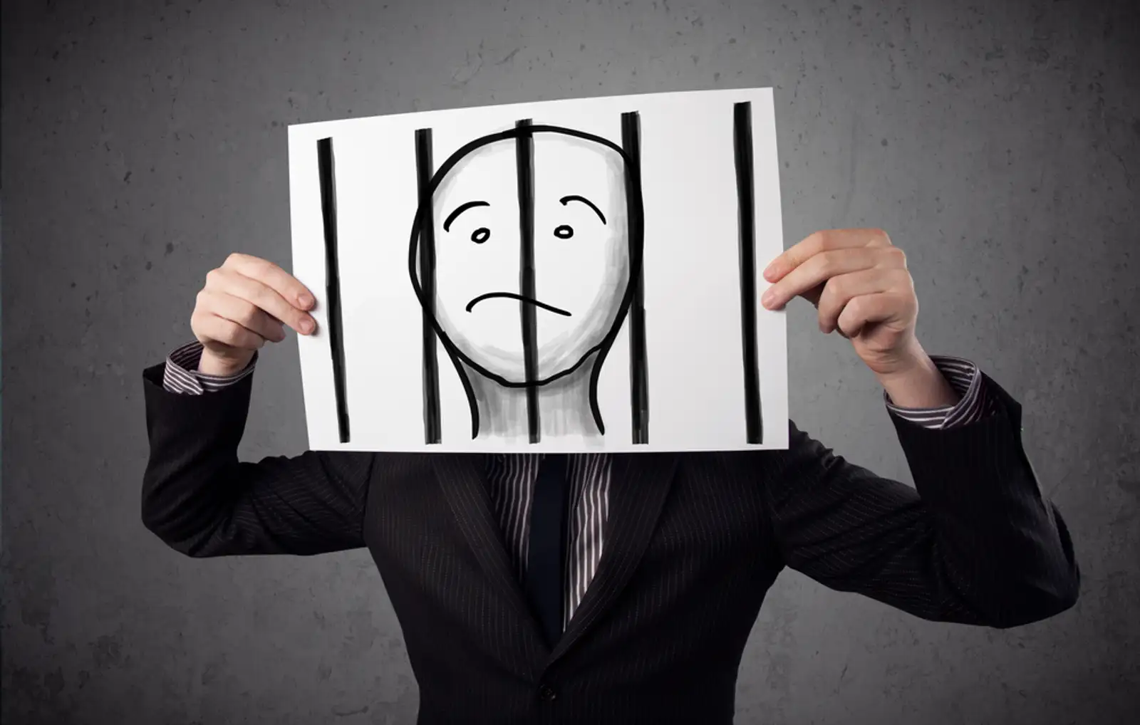 Businessman holding a paper with a prisoner in jail behind the bars on it in front of his head.jpeg
