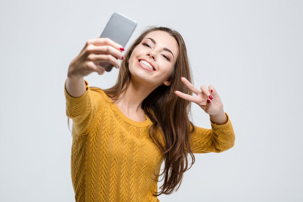 Portrait of a smiling cute woman making selfie photo on smartphone isolated on a white background.jpeg