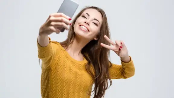 Portrait of a smiling cute woman making selfie photo on smartphone isolated on a white background.jpeg
