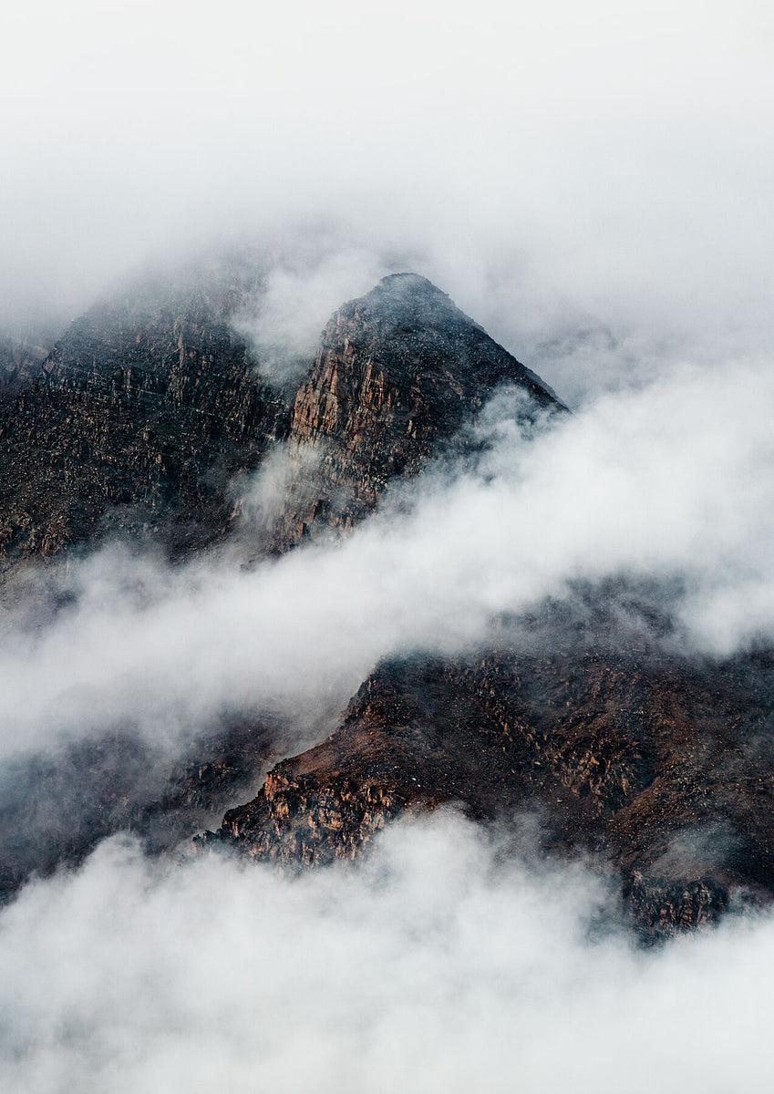 Rocky mountain peaks emerging through dense white clouds.