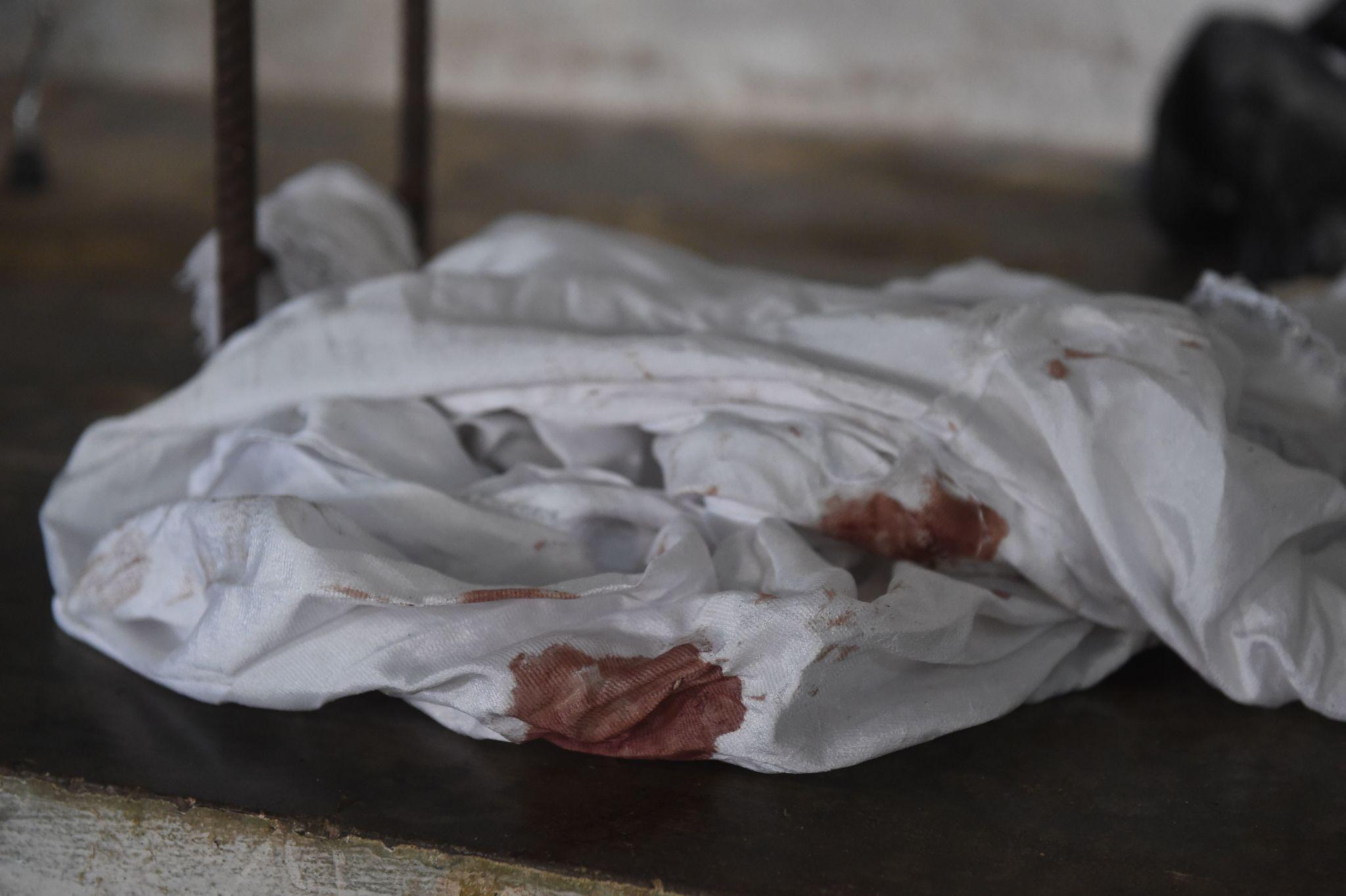A white agbada stained with blood and lying on dark earth.