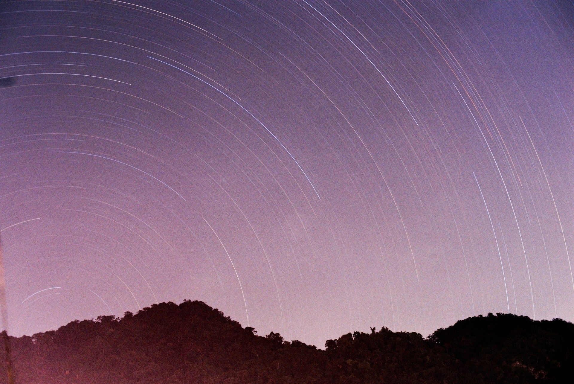 Star trails arc across a purple night sky over mountains