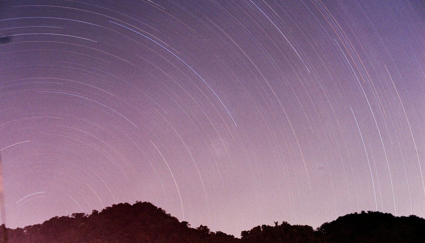 Star trails arc across a purple night sky over mountains