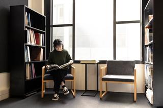 A woman sitting by herself reading a book with a chair and table next to her and book cases on either side