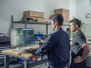 two people at a computer with code on the monitor