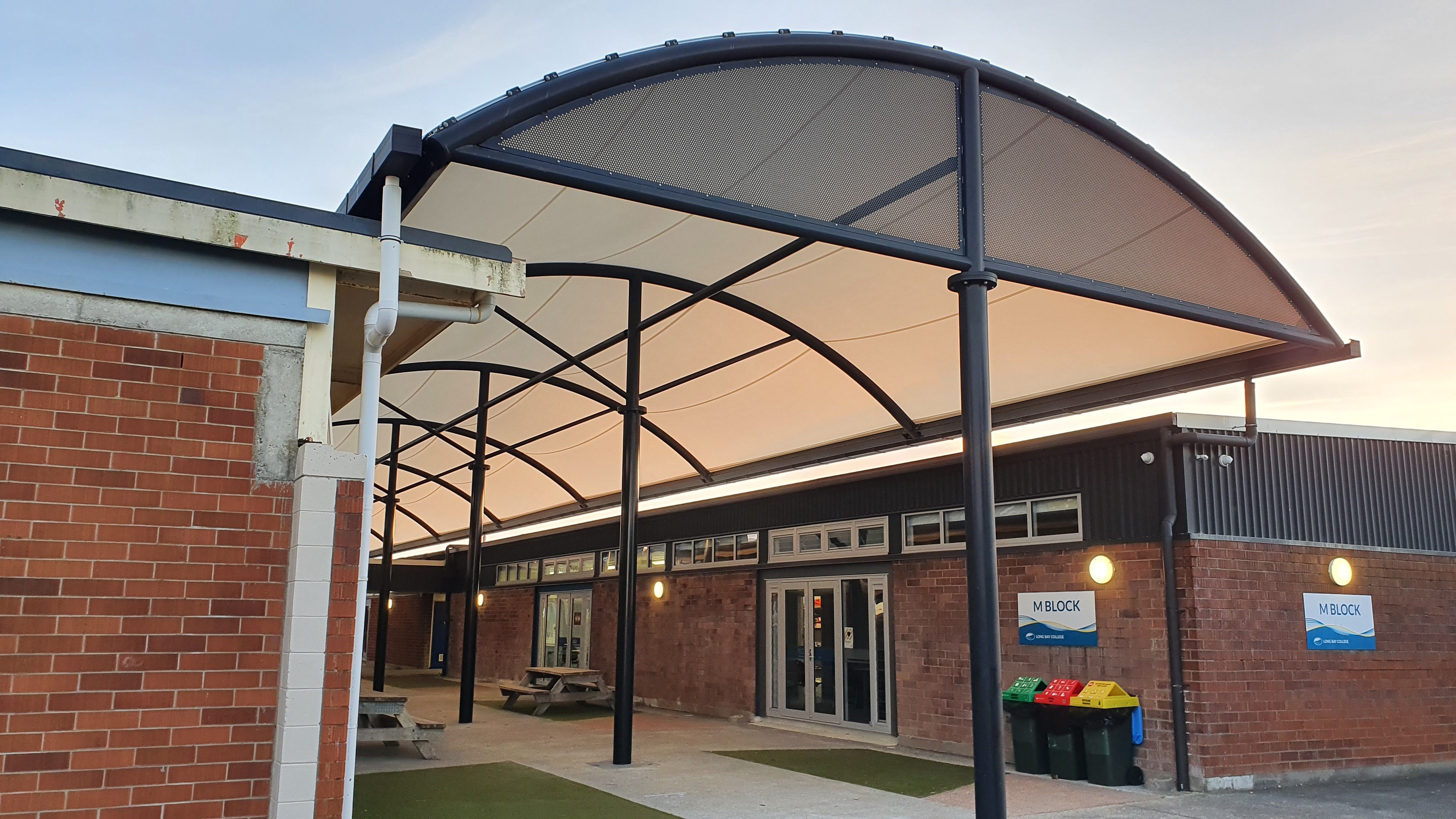 A large rounded outdoor shade covering a school walk way with brick buildings either side 