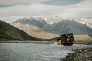 A utility vehicle crossing a river with mountains in the background 