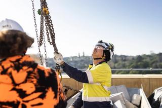 A construction worker on site guiding chains suspended by a crane