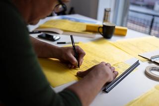 Over the shoulder of a man designing something on yellow piece of paper