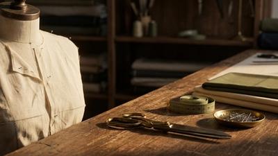 Plain muslin toile pinned on a tailor's dress form beside brass shears in warm workshop light