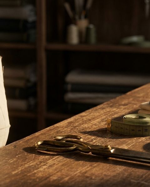 Plain muslin toile pinned on a tailor's dress form beside brass shears in warm workshop light