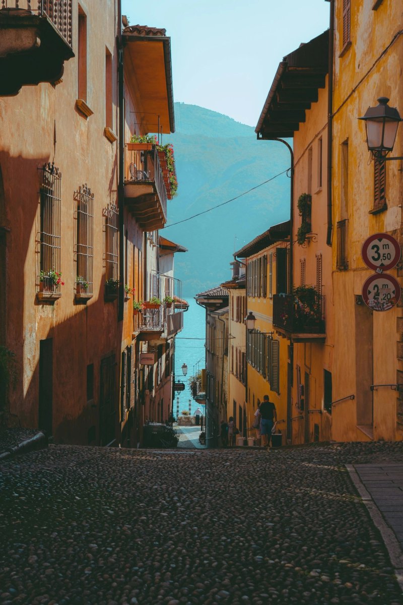Narrow cobblestone street between colorful buildings leading to Lake Maggiore