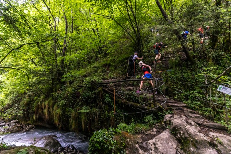 UTLAC trail runners crossing a rope bridge through lush forest above Lake Como