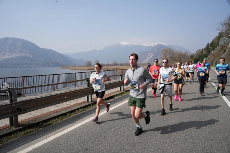 Runners along the lakeside road during the Lago Maggiore Half Marathon with snow-capped mountains in the background