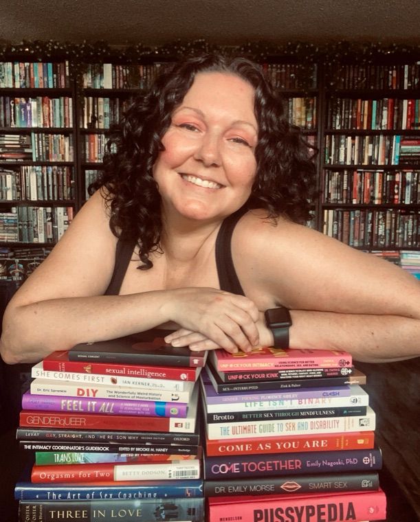 Niki Geroni-Lajoie, smiling, leaning on a stack of books about sex and relationships