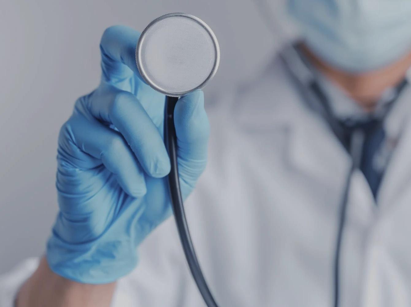 Doctor en guantes azules sosteniendo un estetoscopio