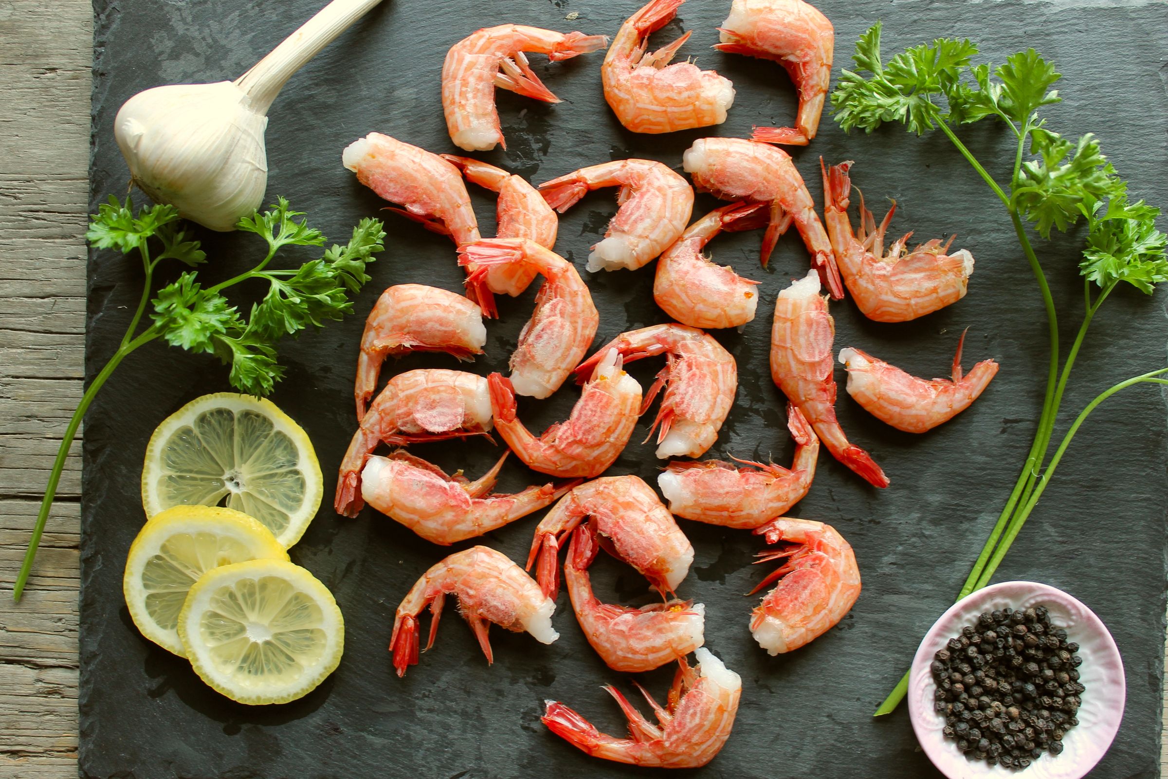 a pile of shrimp, lemon slices, parsley, garlic and black pepper on a cutting board