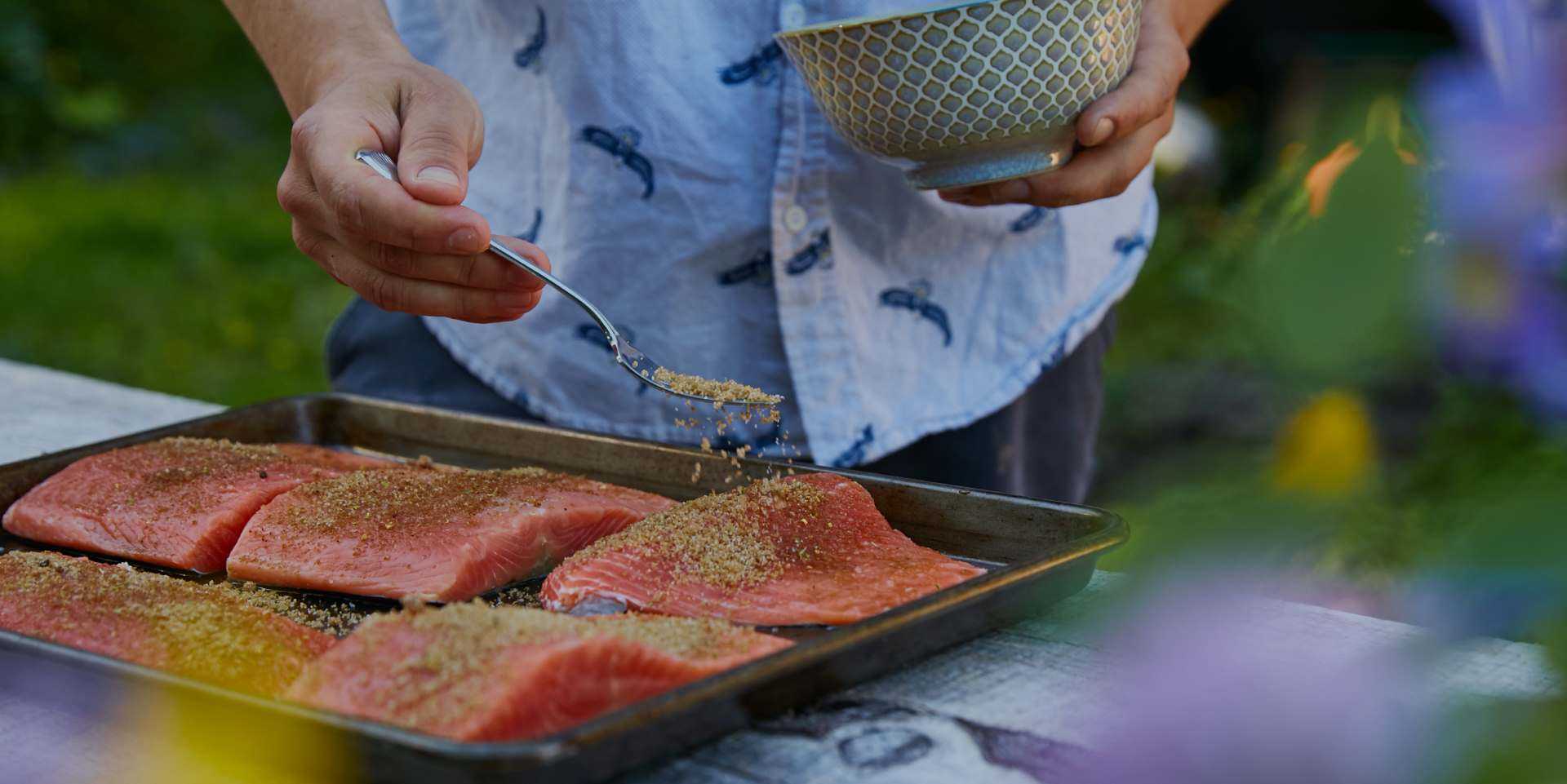 person seasoning salmon to put on a grill