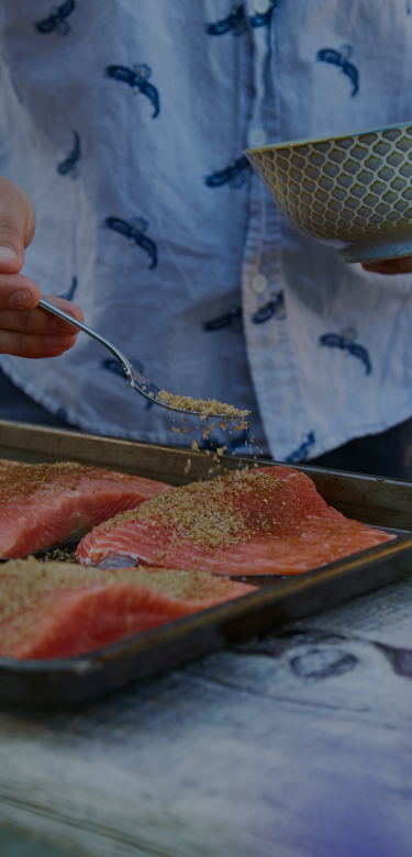 person seasoning salmon to put on a grill