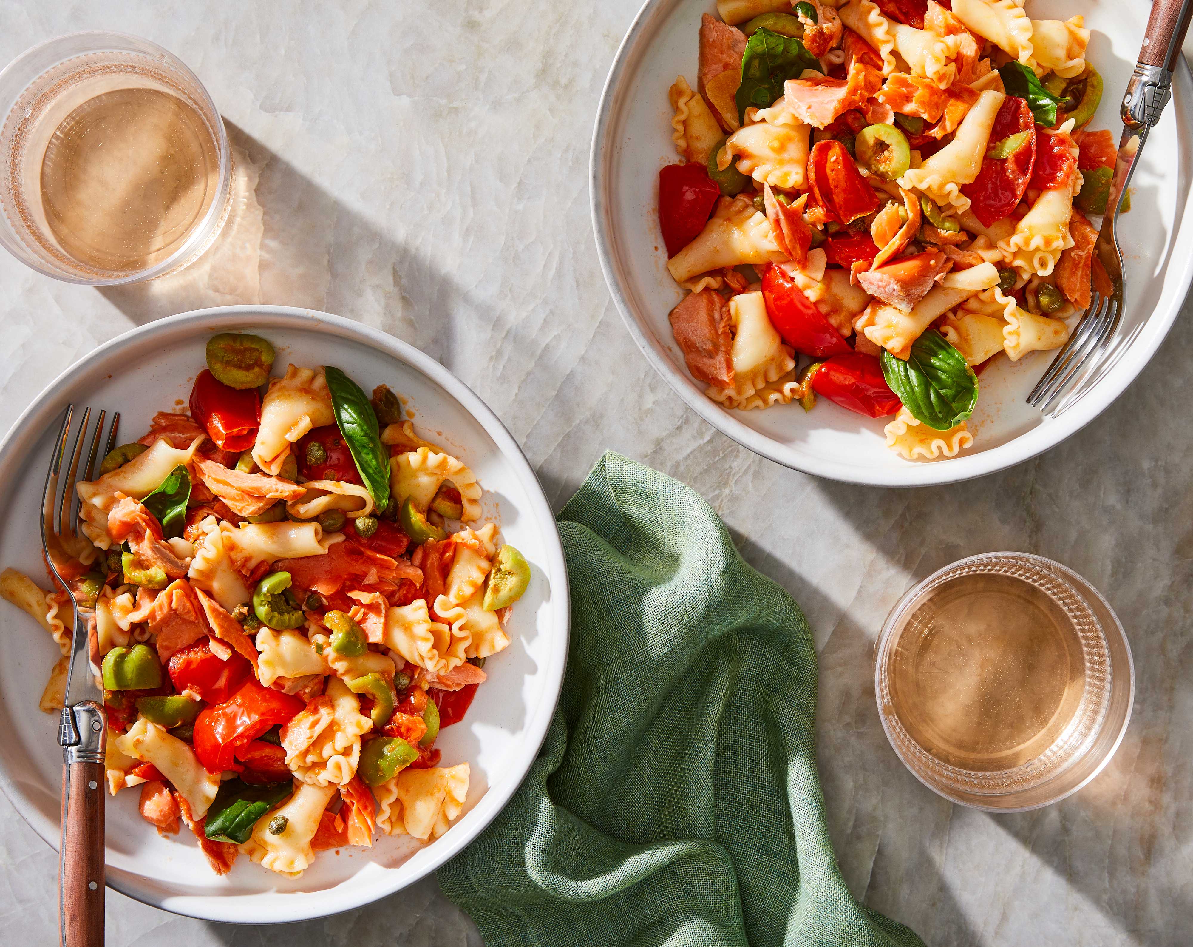 two bowls with pasta, tomatoes, olives, and salmon wit two wine glasses