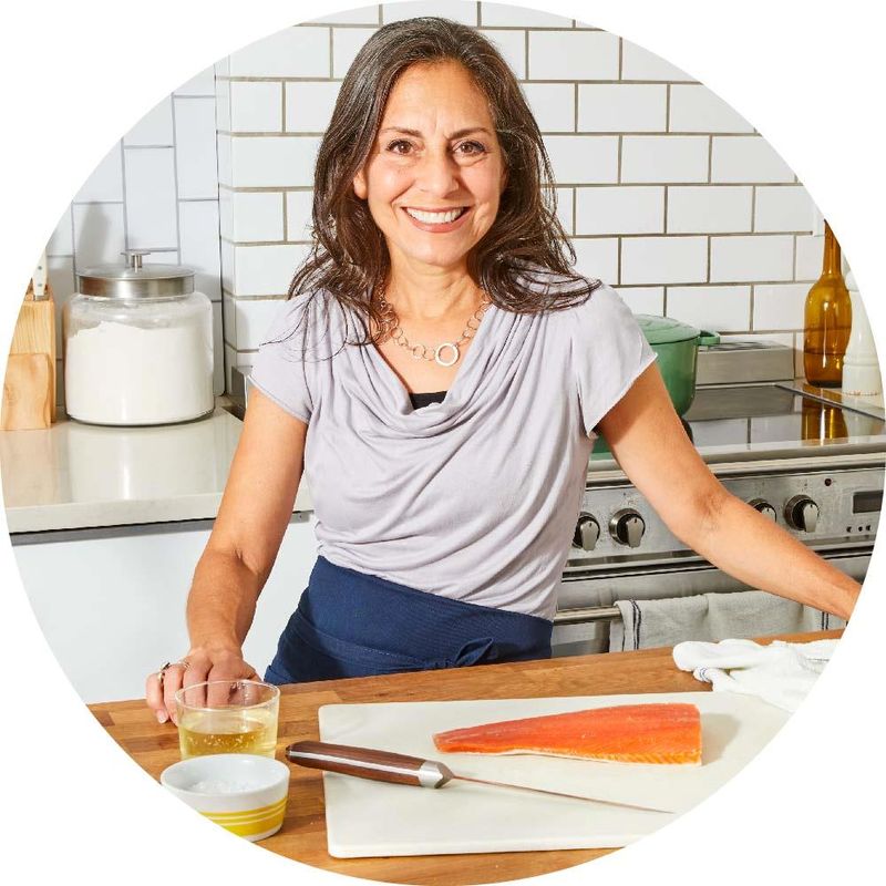 a woman is standing in kitchen cutting a piece of salmon on a cutting board