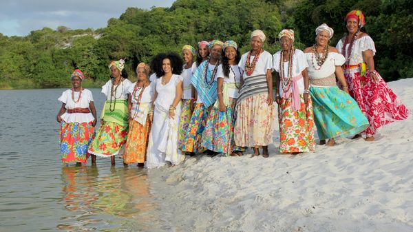 Ganhadeiras de Itapuã com a cantora Mariene de Castro sentadas na areia da Lagoa do Abaeté