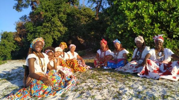 Ganhadeiras de Itapuã sentadas em semi-círculo na areia, sorriem para a câmera.