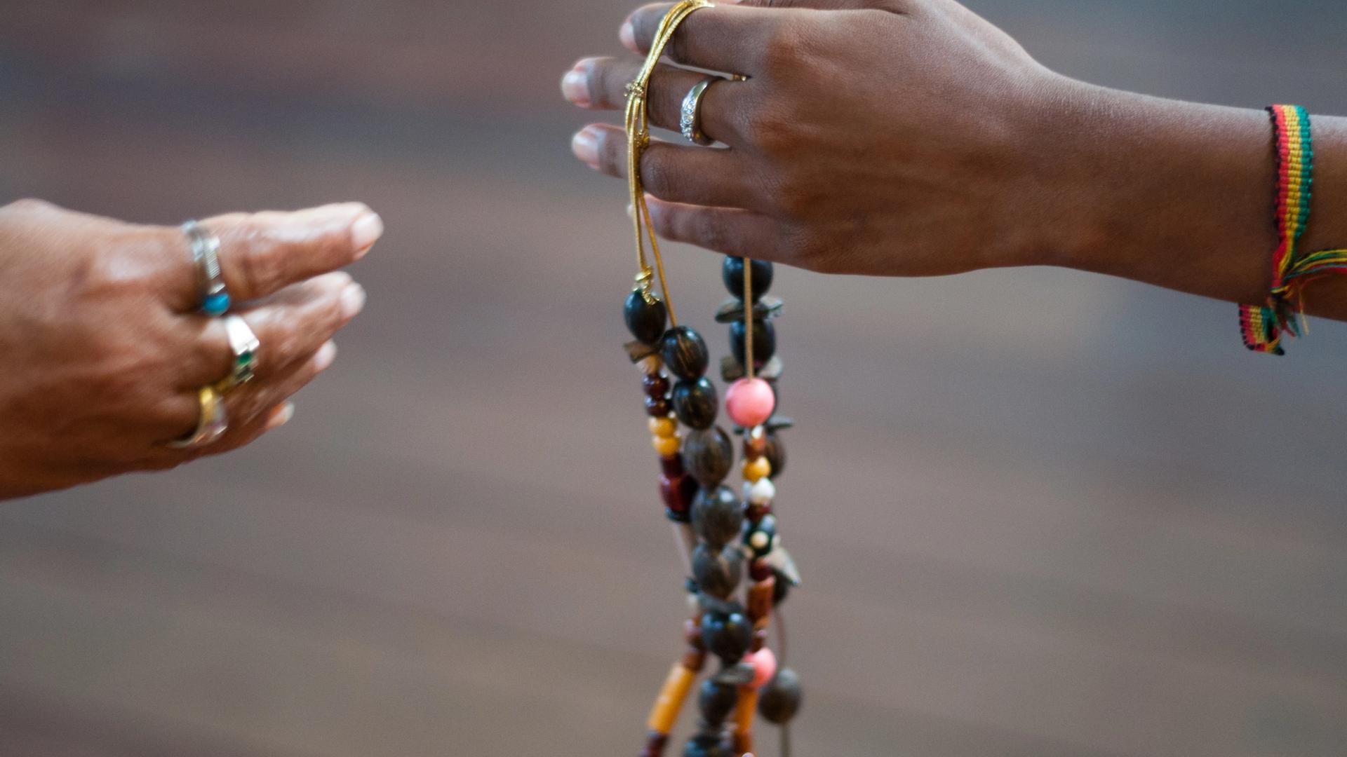 Uma mão se estende para outra oferecendo um colar de contas.