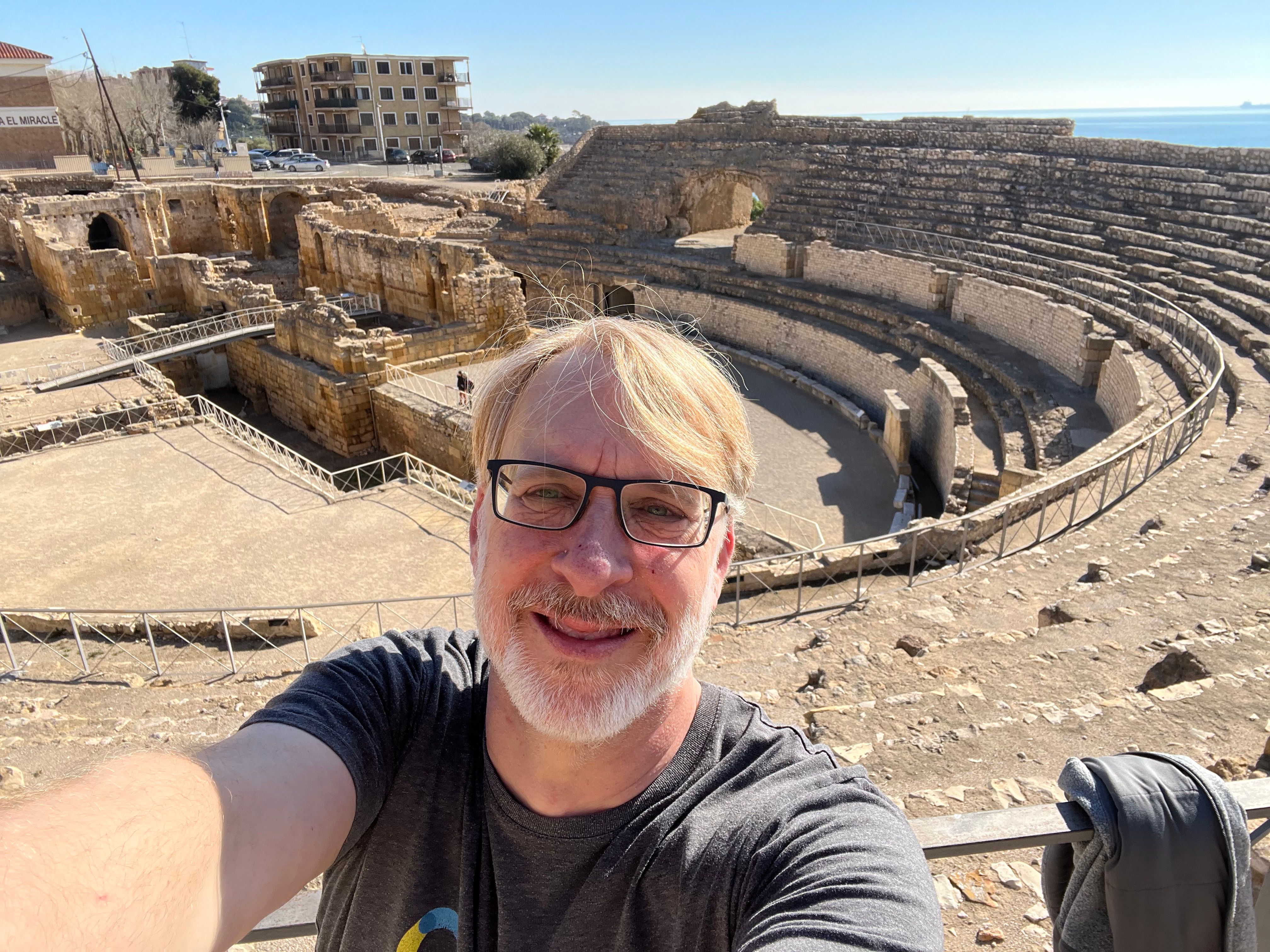 Rusty Cole taking a selfie in front of ancient Roman amphitheater ruins with the sea in the distance.