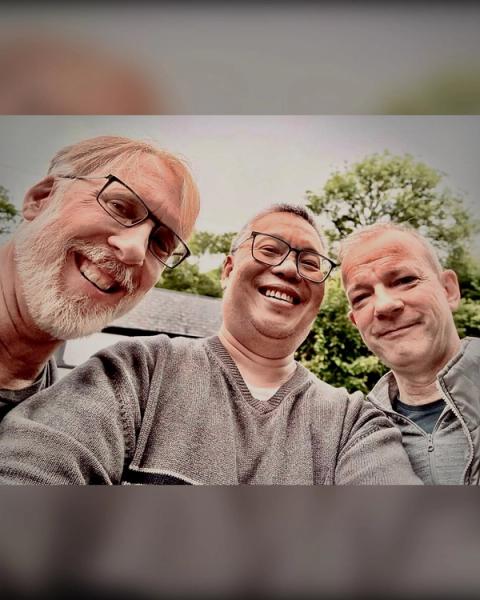 A selfie of three smiling men, all wearing glasses, outdoors.