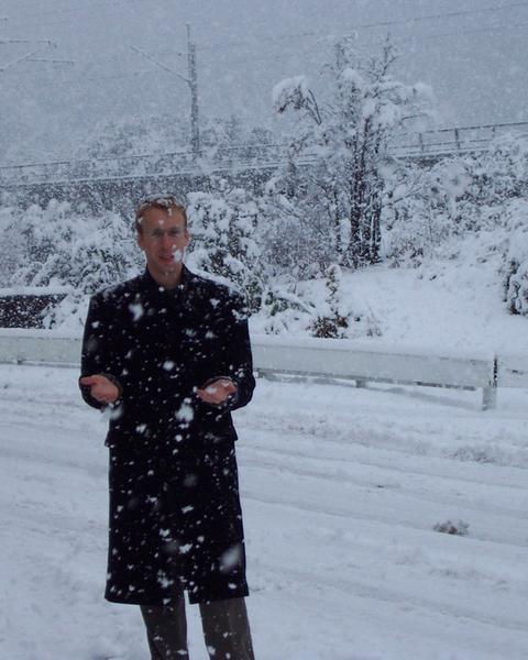 Rusty Cole standing in heavy snowfall in a long black coat.