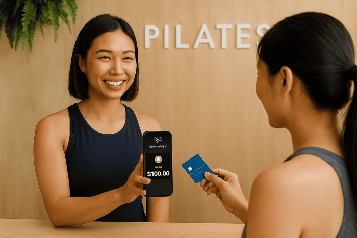 A boutique studio owner accepting an in-person payment using their phone as a contactless payment terminal at the front desk.