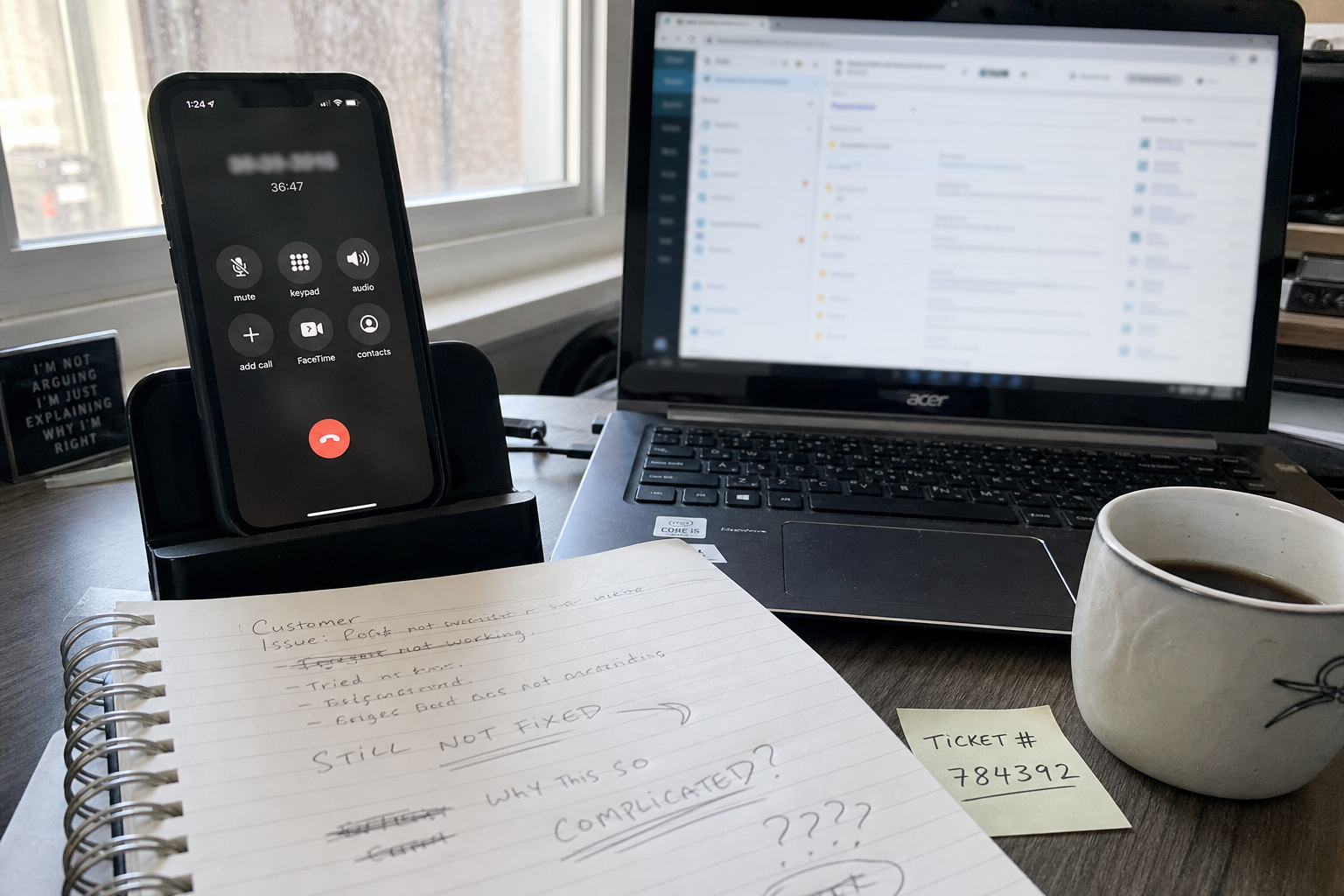 Studio operator desk during a long support call with phone showing extended hold time, frustrated notes on the desk, and a half-empty coffee mug