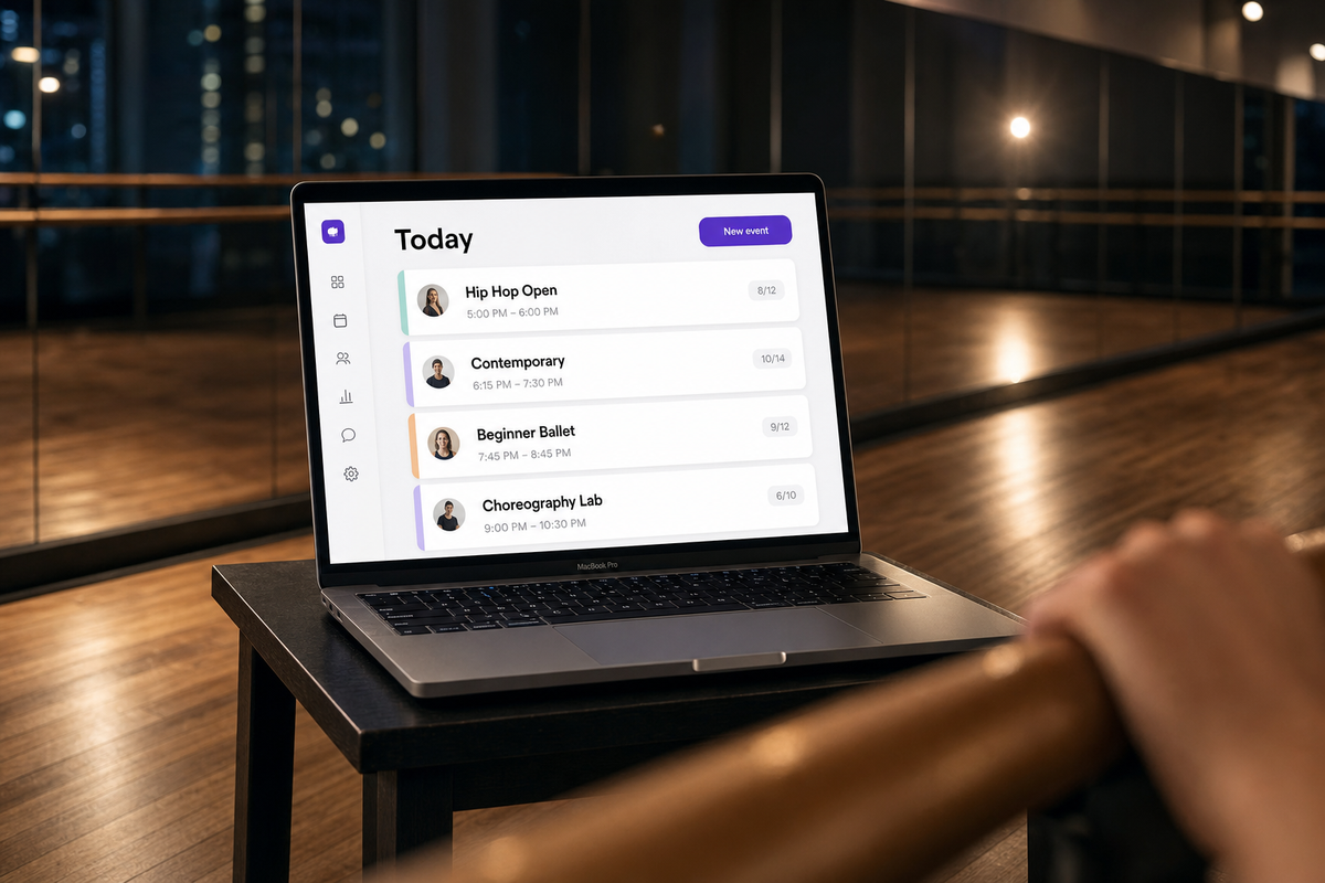 Cinematic shot through a polished ballet barre toward a MacBook on a dark wooden stand displaying the Vibefam class schedule (Hip Hop Open, Contemporary, Beginner Ballet, Choreography Lab) in a sleek dance studio at evening.